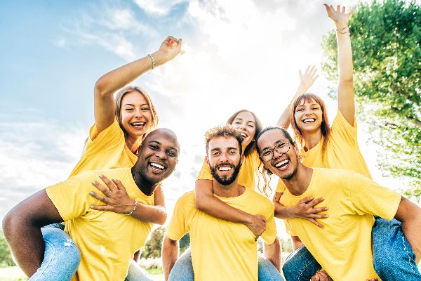 Junge multikulturelle Menschen in gelben Leiberln, lachend, tragen sich huckepack